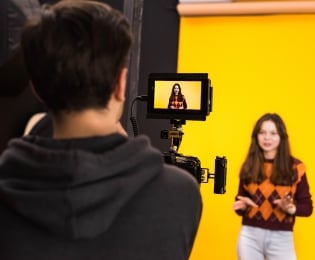 Students in a TV studio. One operating the camera for the other in front. 