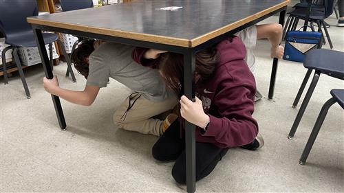Student practicing duck, cover, and hold on underneath a sturdy surface.